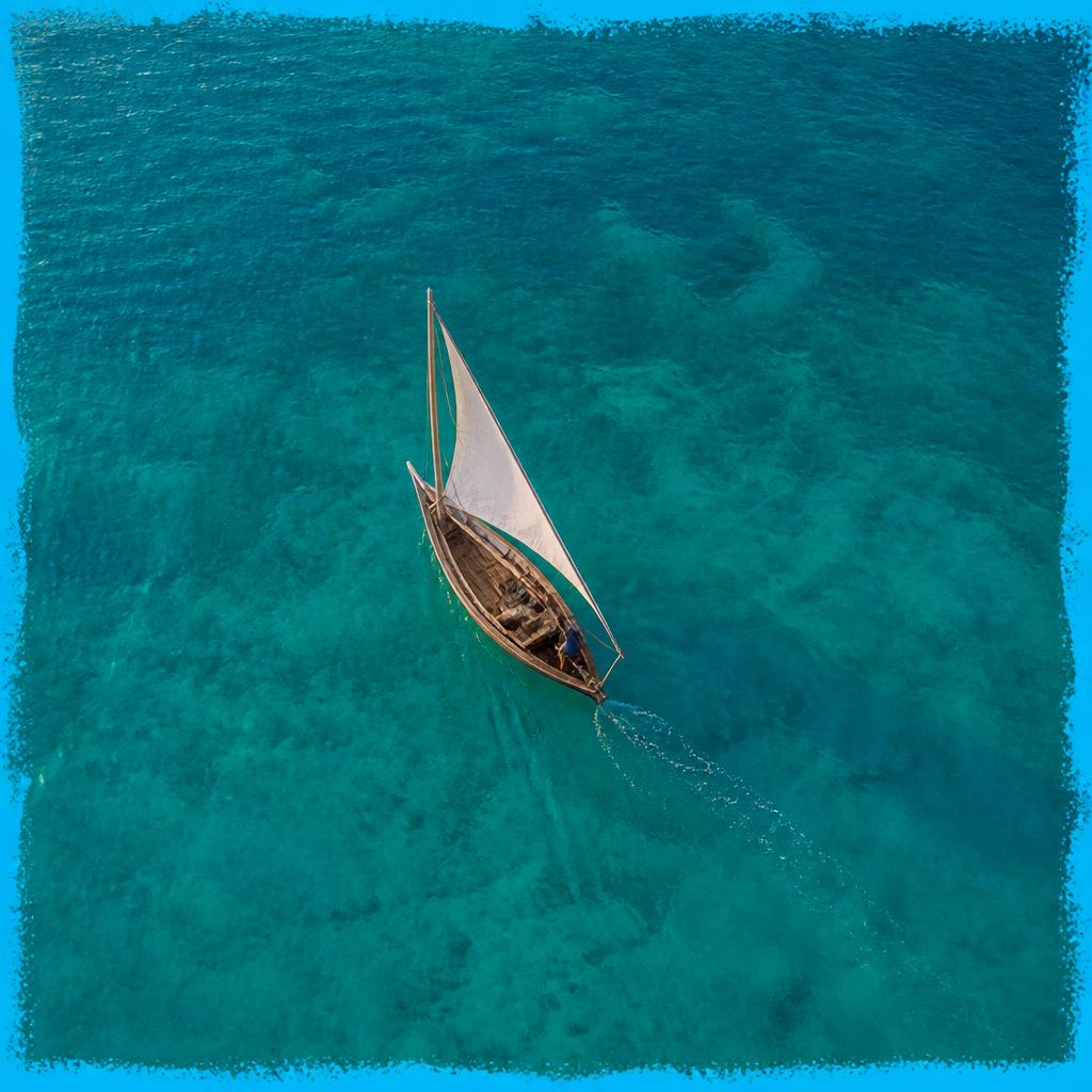 A small sailboat seen from above on calm turquoise ocean water